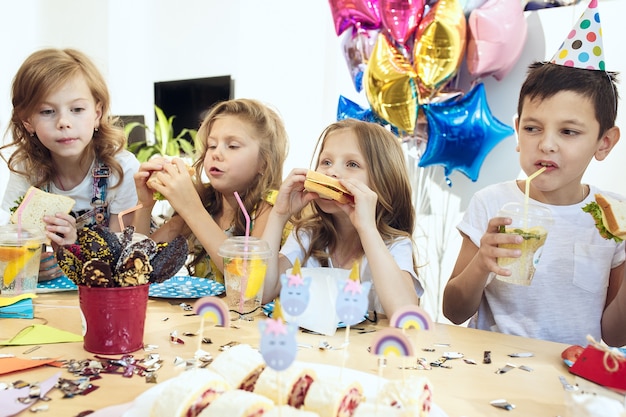 children and birthday decorations. boys and girls at table setting with food, cakes, drinks and party gadgets.