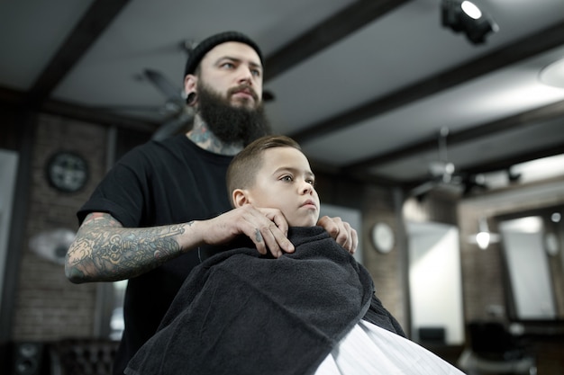 Children hairdresser cutting little boy against a dark background.