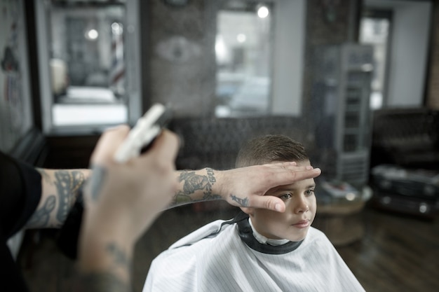 Children hairdresser cutting little boy against a dark