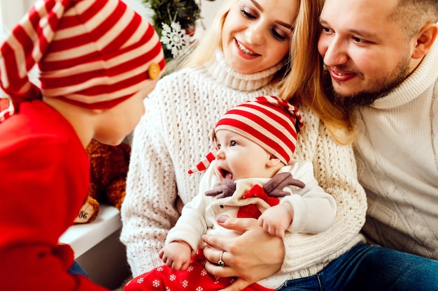 Children play sitting on parents' knees in a room decorated for Christmas eve 