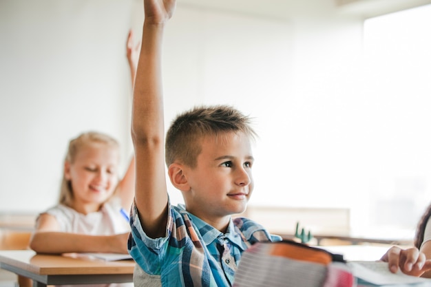 Free photo children sitting at school desks raising hands