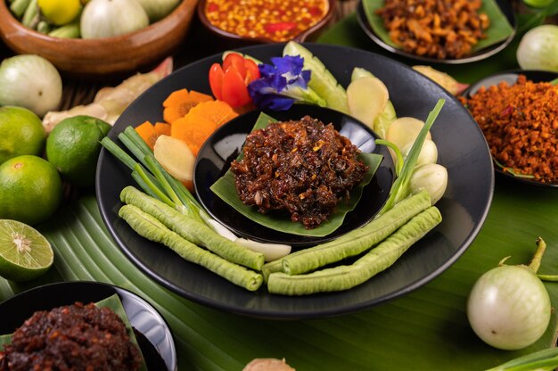 Chili paste is served on banana leaves on a plate with long beans, lime, chili, and eggplant.