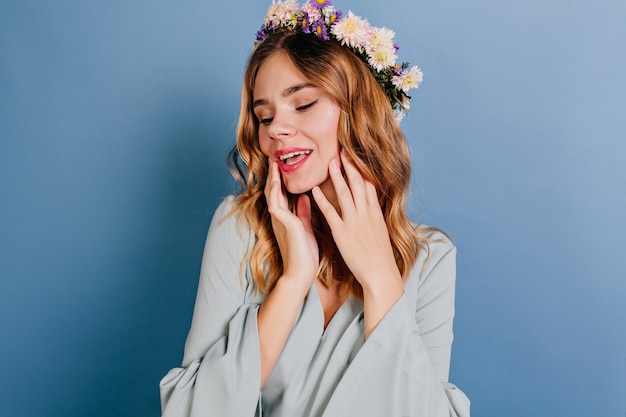 Chilling european woman in flower wreath posing on blue wall