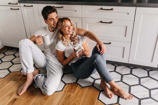 Chilling young people drinking coffee in weekend morning. Indoor portrait of smiling couple relaxing during breakfast.