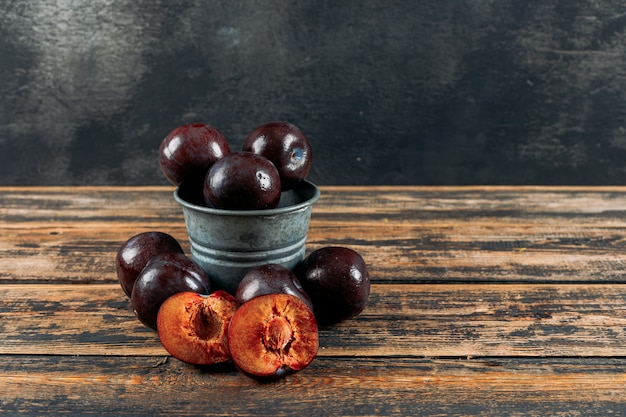 Chilly plums in a small backet on a dark wooden and dark grey background. side view.