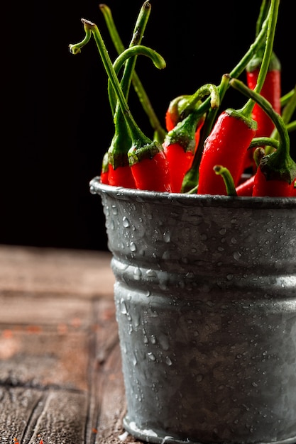 Free photo chilly red peppers in a mini bucket close-up on stone tile and black