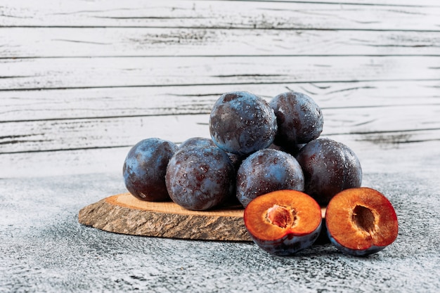 Free Photo chilly sliced plums in a wooden board on grey stucco background, side view.