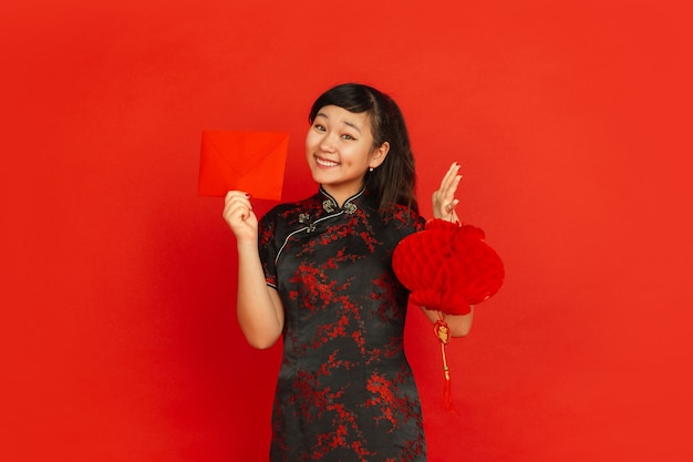 Free Photo chinese new year 2020. asian young girl's portrait isolated on red background. female model in traditional clothes looks happy with decoration and red envelope. celebration, holiday, emotions.