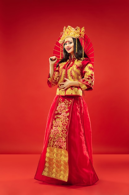 Free Photo chinese traditional graceful woman at studio over red background. beautiful girl wearing national costume. chinese new year, elegance, grace, performer, performance, dance, actress, dress concept