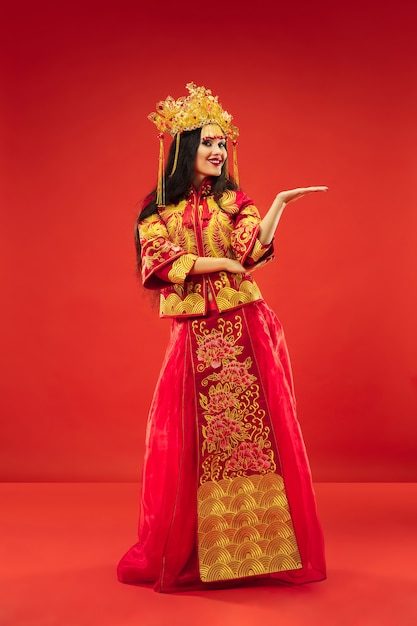 Free Photo chinese traditional graceful woman at studio over red background. beautiful girl wearing national costume. chinese new year, elegance, grace, performer, performance, dance, actress, dress concept