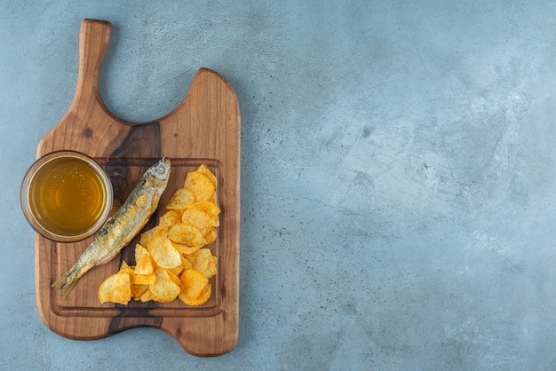 Free photo chips, fish and glass of beer on a board , on the marble background.