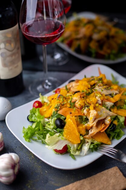 chips orange salad with sliced vegetables along with red wine on grey desk