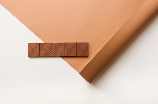 Free photo chocolate bar on rolled up card paper against white backdrop