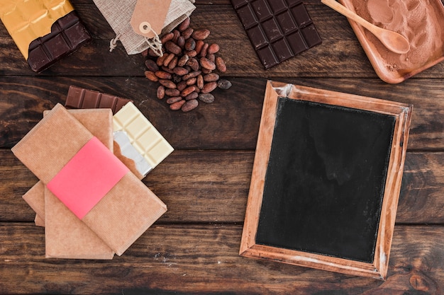 Chocolate bar stack, blank wooden slate, cocoa beans and powder on table