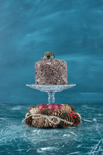 Free photo chocolate cake on a pedestal and a pine cone wreath on blue.