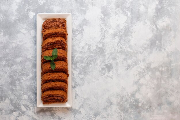 Chocolate cake roll with cocoa powder on white plate,top view