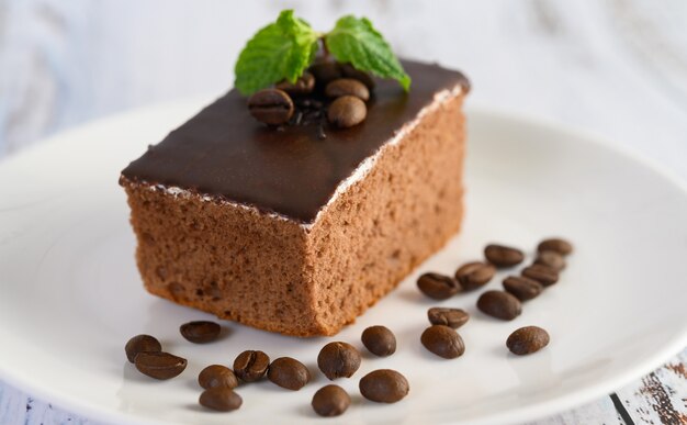 Chocolate cake on a white plate with coffee beans on a wooden table