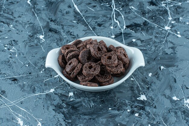 Chocolate coated corn ring in a bowl, on the marble background. 