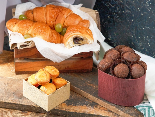 Chocolate croissants, box of pralines and muffins on a piece of wood