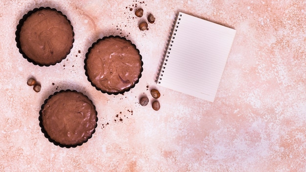 Free photo chocolate cupcake; hazelnut and spiral notepad on textured background