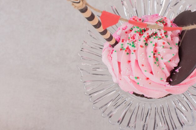 Chocolate cupcake with frosting and sprinklers on glass.