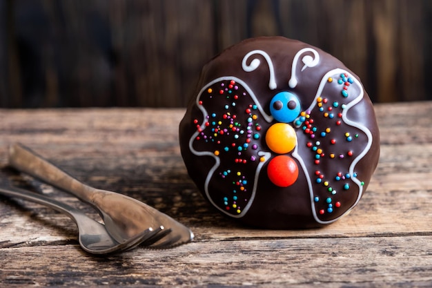 Free photo chocolate donut with a shaped butterfly on a wooden rustic board and asilver metallic fork and knife