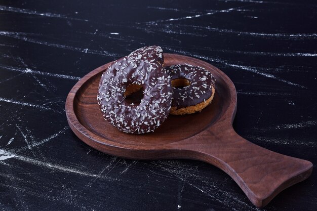 Chocolate doughnuts isolated on black surface in a wooden platter. 