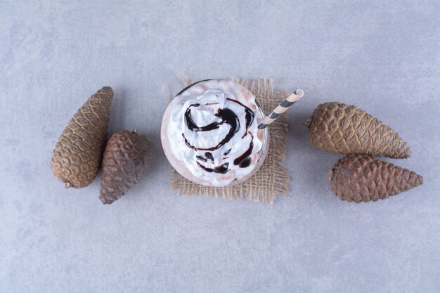 Chocolate milkshake with whipped cream and pine cone on marble table.