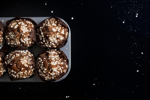 Free photo chocolate muffins in paper cupcake holder on baking tray against black backdrop