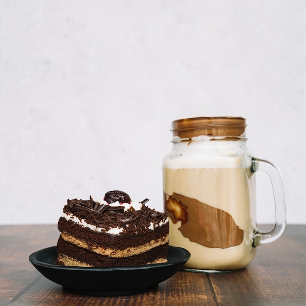 Chocolate smoothie in jar with slice of cake on wooden table