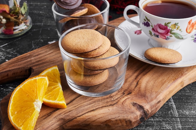 Chocolate sponge cookies on a wooden board with orange and tea. 