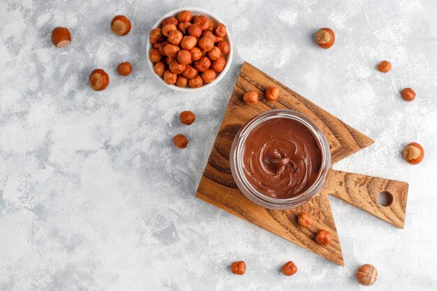 Chocolate spread or nougat cream with hazelnuts in glass jar on concrete ,  copyspace