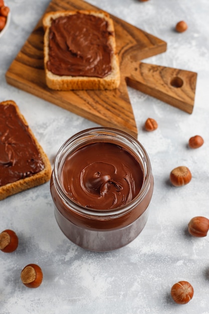 Free photo chocolate spread or nougat cream with hazelnuts in glass jar on concrete ,  copyspace