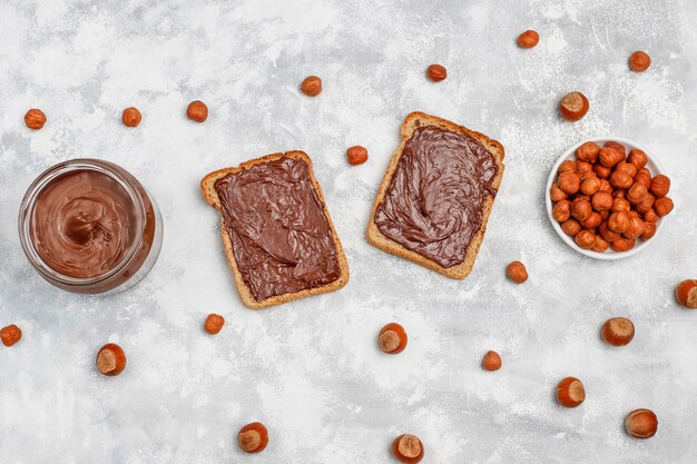 Chocolate spread or nougat cream with hazelnuts in glass jar on concrete ,  copyspace