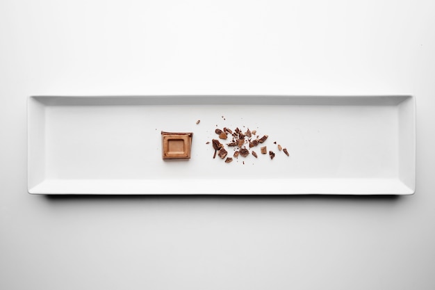 Free Photo chocolate square piece and crumbles isolated in center rectangular ceramic plate on white table background