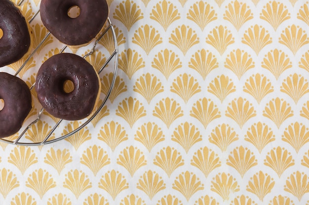 Free photo chocolates donuts on metal rack over the golden wallpaper