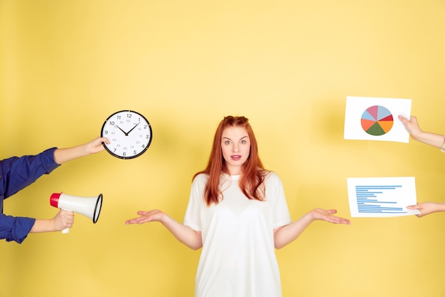 Choosing. Caucasian young woman's portrait on yellow studio background, too much tasks. How to manage time right. Concept of office working, business, finance, freelance, self management, planning.