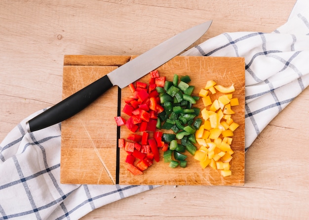 Chopped bell peppers on chopping board with knife and tablecloth over the wooden table