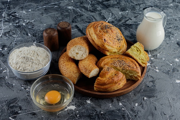 Chopped Turkish bagel simit with uncooked chicken egg and a glass pitcher of milk. 