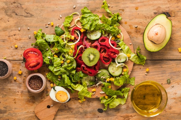 Free photo chopped vegetables and fruit on chopping board with ingredients; boiled egg and oil on wooden backdrop