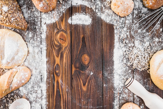 Free photo chopping board frame with spread flour and surrounded bread loaves