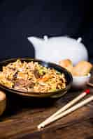 Free photo chopsticks and bowl of delicious noodles with beef on wooden desk