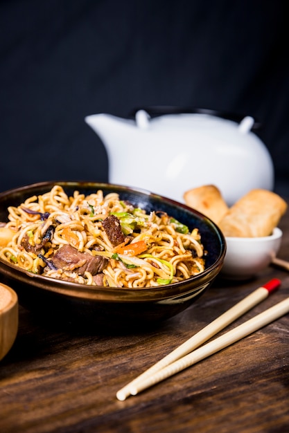 Chopsticks and bowl of delicious noodles with beef on wooden desk