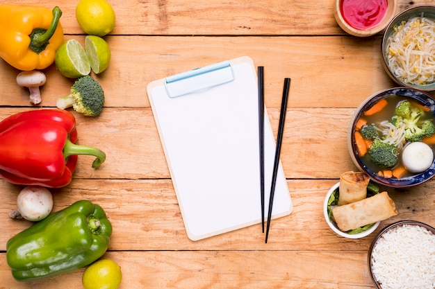 Free photo chopsticks on clipboard between the vegetables and thai traditional food on wooden plank