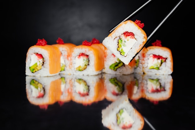 Chopsticks holding sushi roll Philadelphia on black background made of salmon