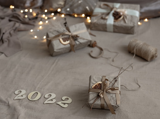 Free Photo christmas background with gift boxes wrapped in craft paper and wooden numbers 2022 on blurred background with garland.