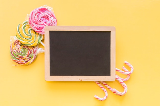 Christmas candy canes and lollipops behind the wooden slate over the yellow background