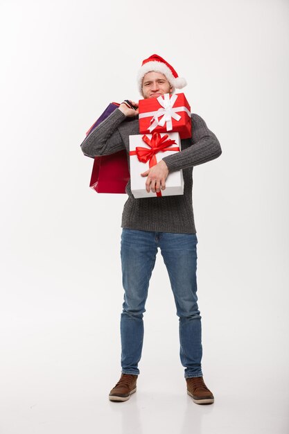 Christmas Concept young handsome man with beard holding heavy presents and shopping bags with exhausted facial expression on white background