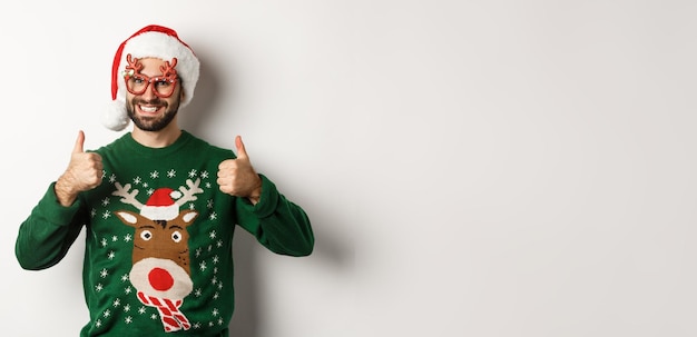 Free Photo christmas holidays celebration concept happy man in santa hat and party glasses showing thumbs up in