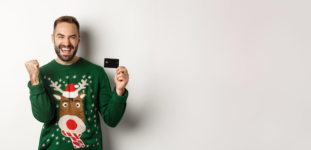 Free photo christmas holidays and shopping concept excited man showing credit card and looking happy standing o